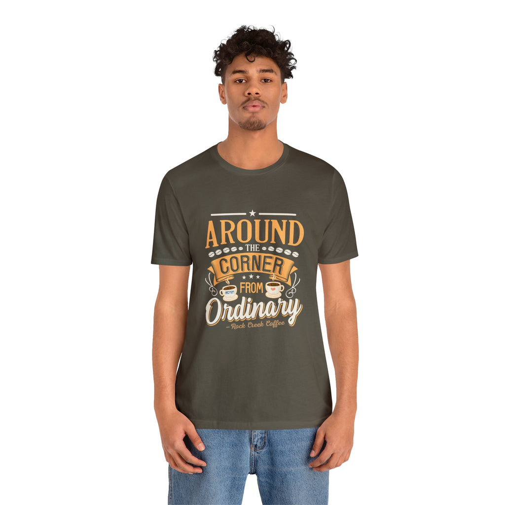 Adult man modeling an army green short-sleeve T-shirt featuring the phrase “Around the Corner from Ordinary” in a bold coffee-themed typographic design, shown against a plain white background.