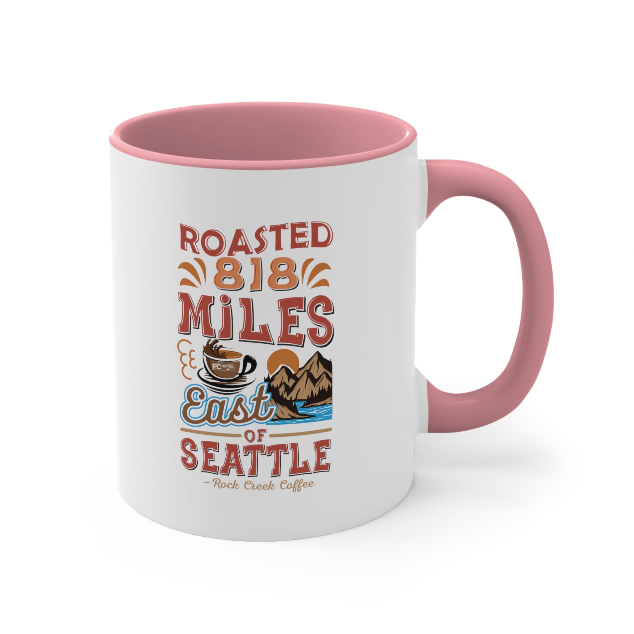 White ceramic coffee mug with a pink interior and handle featuring the Roasted 818 Miles East of Seattle Rock Creek Coffee design in red, blue, and brown lettering with a coffee cup and mountain illustration.