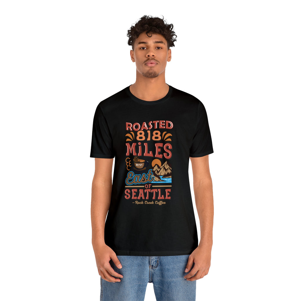Adult man modeling a black short-sleeve Seattle coffee graphic T-shirt reading “Roasted 818 Miles East of Seattle,” shown against a plain white background.