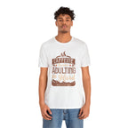 Adult man modeling a white short-sleeve T-shirt featuring the “Caffeine Because Adulting Is Hard” graphic in a stacked typographic design, shown against a plain white background.
