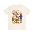 Cream short-sleeve T-shirt laid flat showing a coffee-themed graphic reading “Fueled by Coffee and Dad Jokes” with a steaming coffee cup and illustrated dad holding a mug centered on the front.
