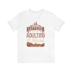 White short-sleeve T-shirt displayed flat against a plain white background, featuring the phrase “Caffeine Because Adulting Is Hard” in a stacked typographic design with coffee-inspired styling and Rock Creek Coffee text below.