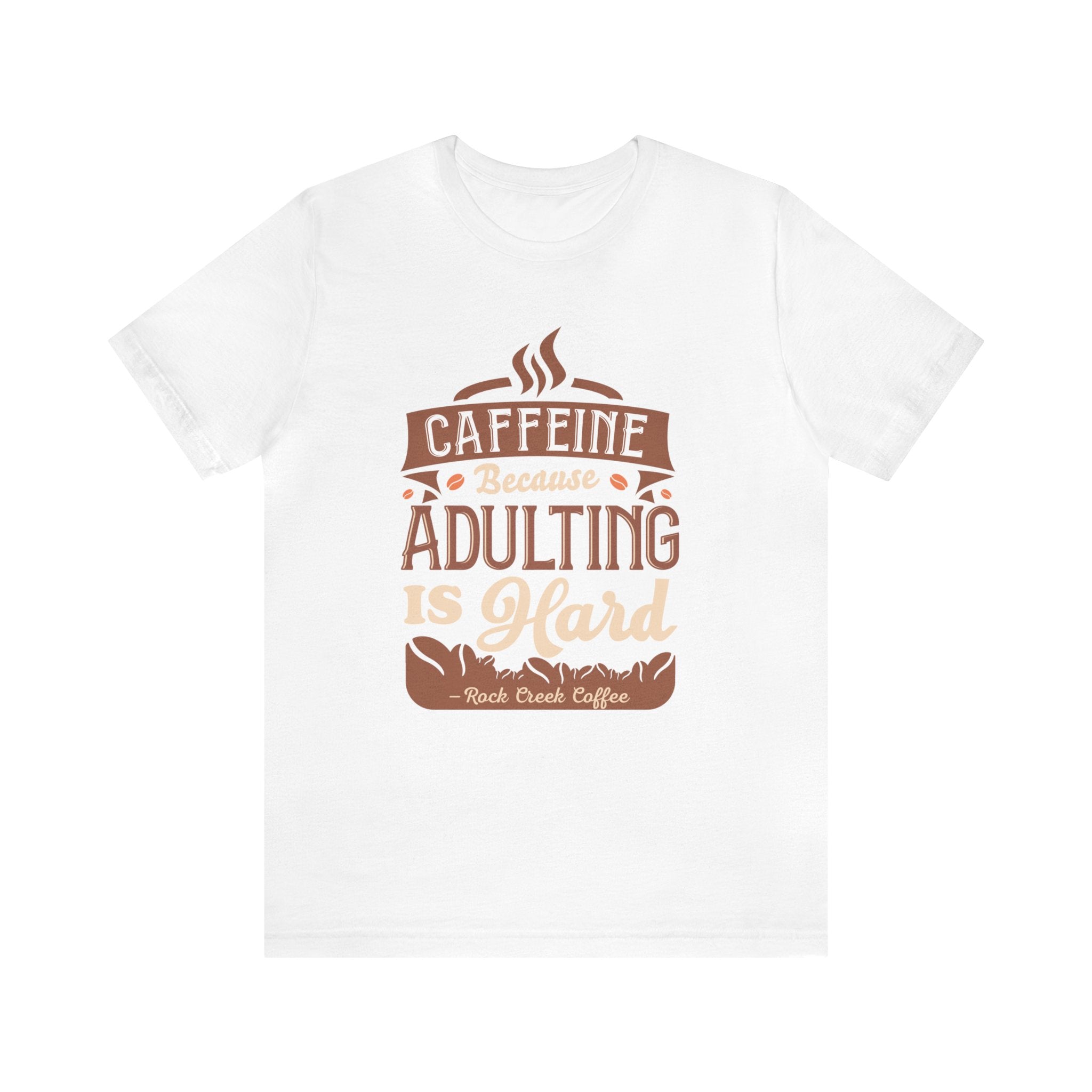White short-sleeve T-shirt displayed flat against a plain white background, featuring the phrase “Caffeine Because Adulting Is Hard” in a stacked typographic design with coffee-inspired styling and Rock Creek Coffee text below.
