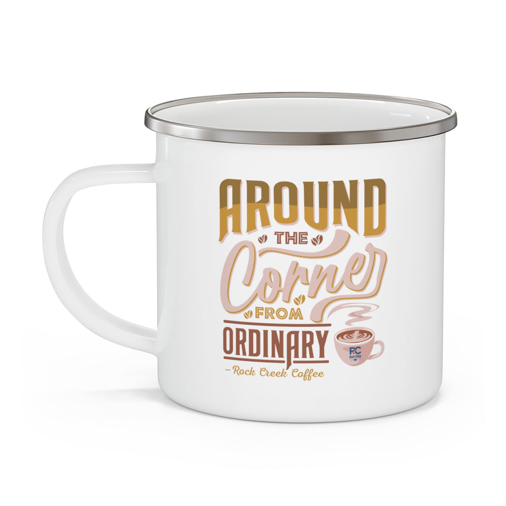 White enamel style coffee mug with silver rim and handle featuring the phrase Around the Corner from Ordinary Rock Creek Coffee in tan, gold, and brown lettering with a small latte cup illustration.