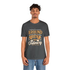 Adult man modeling an asphalt gray short-sleeve T-shirt featuring the “Around the Corner from Ordinary” graphic in a bold coffee-themed typographic design, shown against a plain white background.