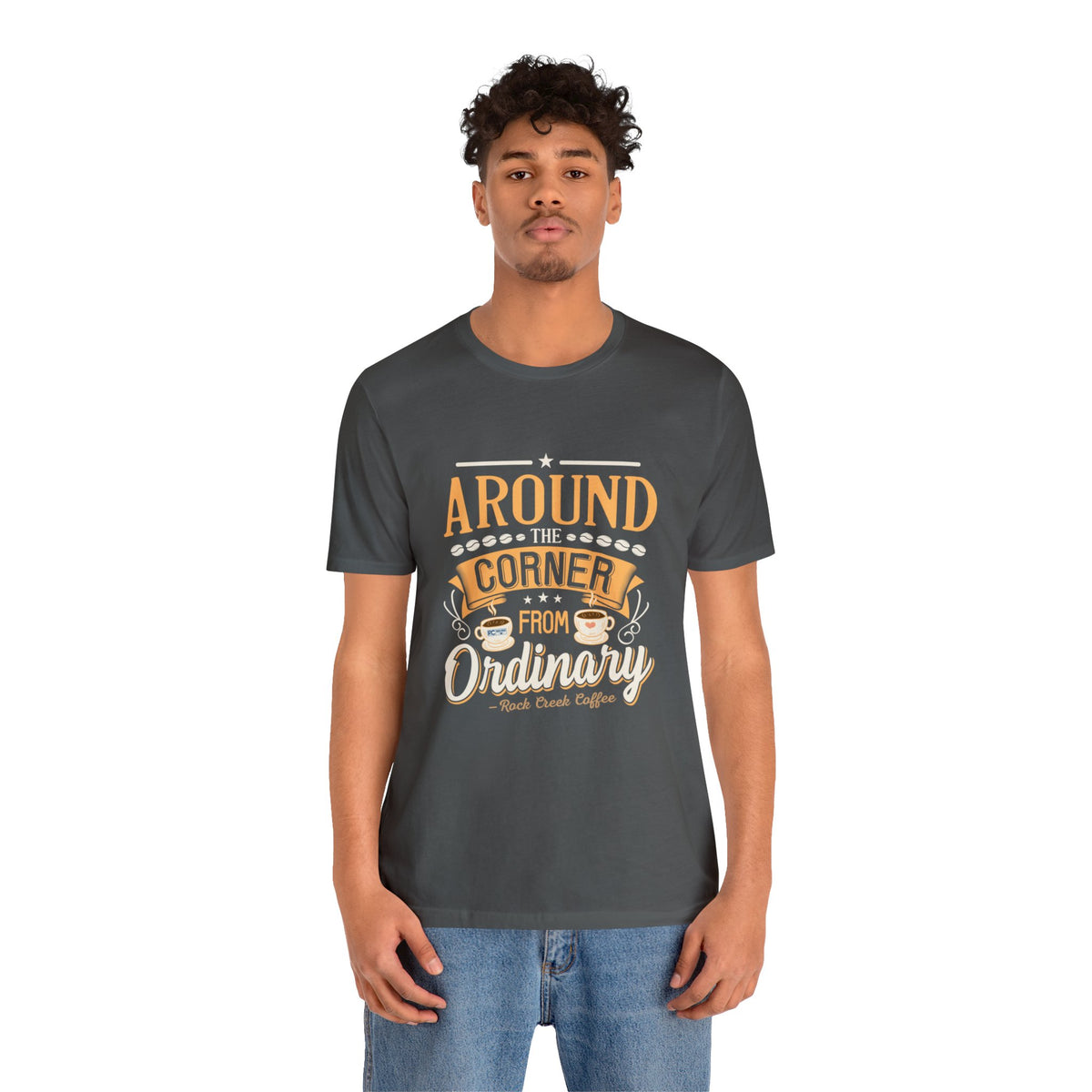Adult man modeling an asphalt gray short-sleeve T-shirt featuring the “Around the Corner from Ordinary” graphic in a bold coffee-themed typographic design, shown against a plain white background.