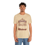 Adult man modeling a soft cream short-sleeve T-shirt featuring the “Caffeine Because Adulting Is Hard” graphic in a stacked typographic design, shown against a plain white background.