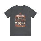 Asphalt short-sleeve T-shirt displayed flat against a plain white background, featuring the “Caffeine Because Adulting Is Hard” graphic in a stacked typographic design with Rock Creek Coffee branding below.