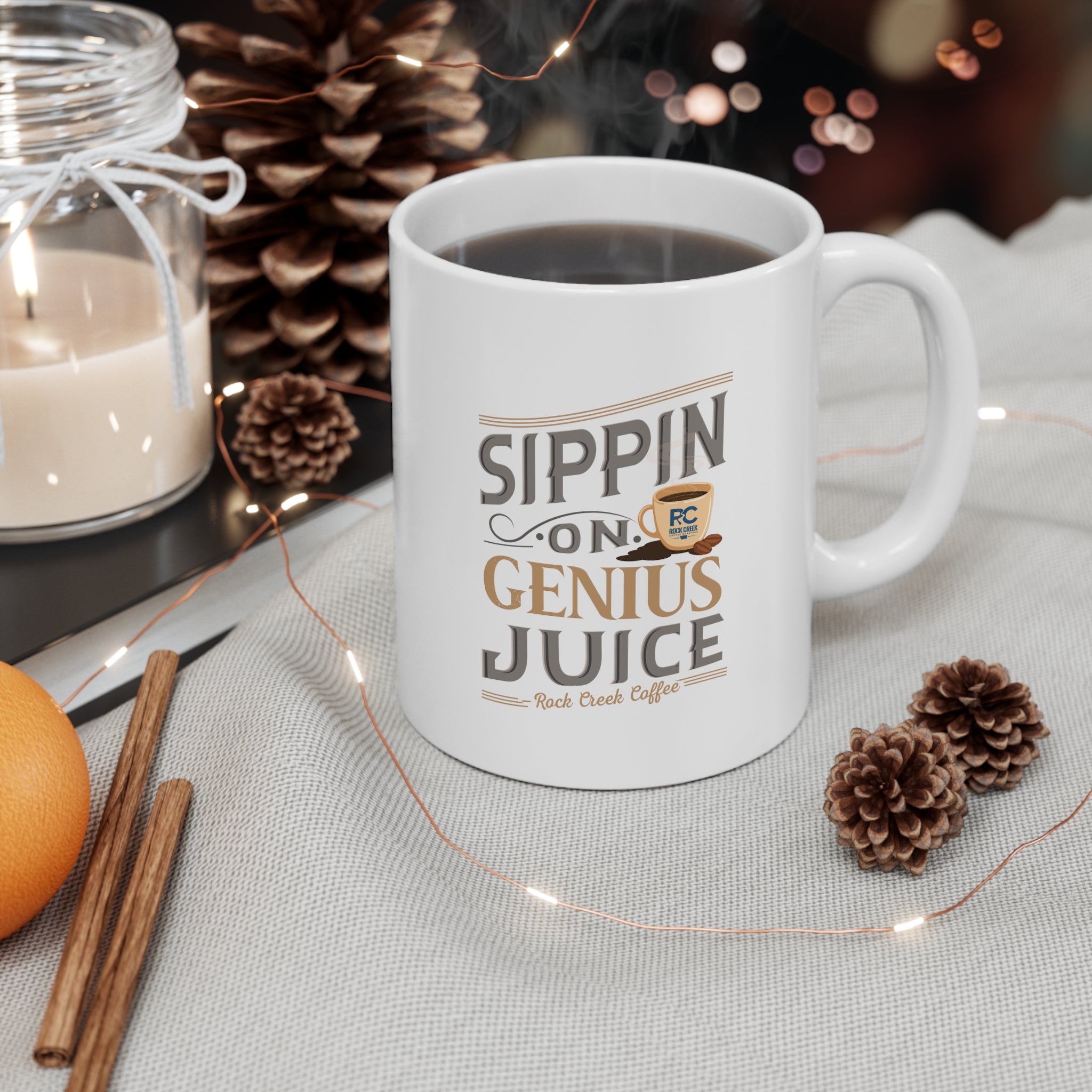 White Rock Creek Coffee mug featuring the phrase “Sippin on Genius Juice” in stylized gray and gold lettering with a small coffee cup graphic, filled with coffee and styled with pumpkins, cinnamon sticks, pinecones, and warm string lights on a cozy fall themed tabletop.