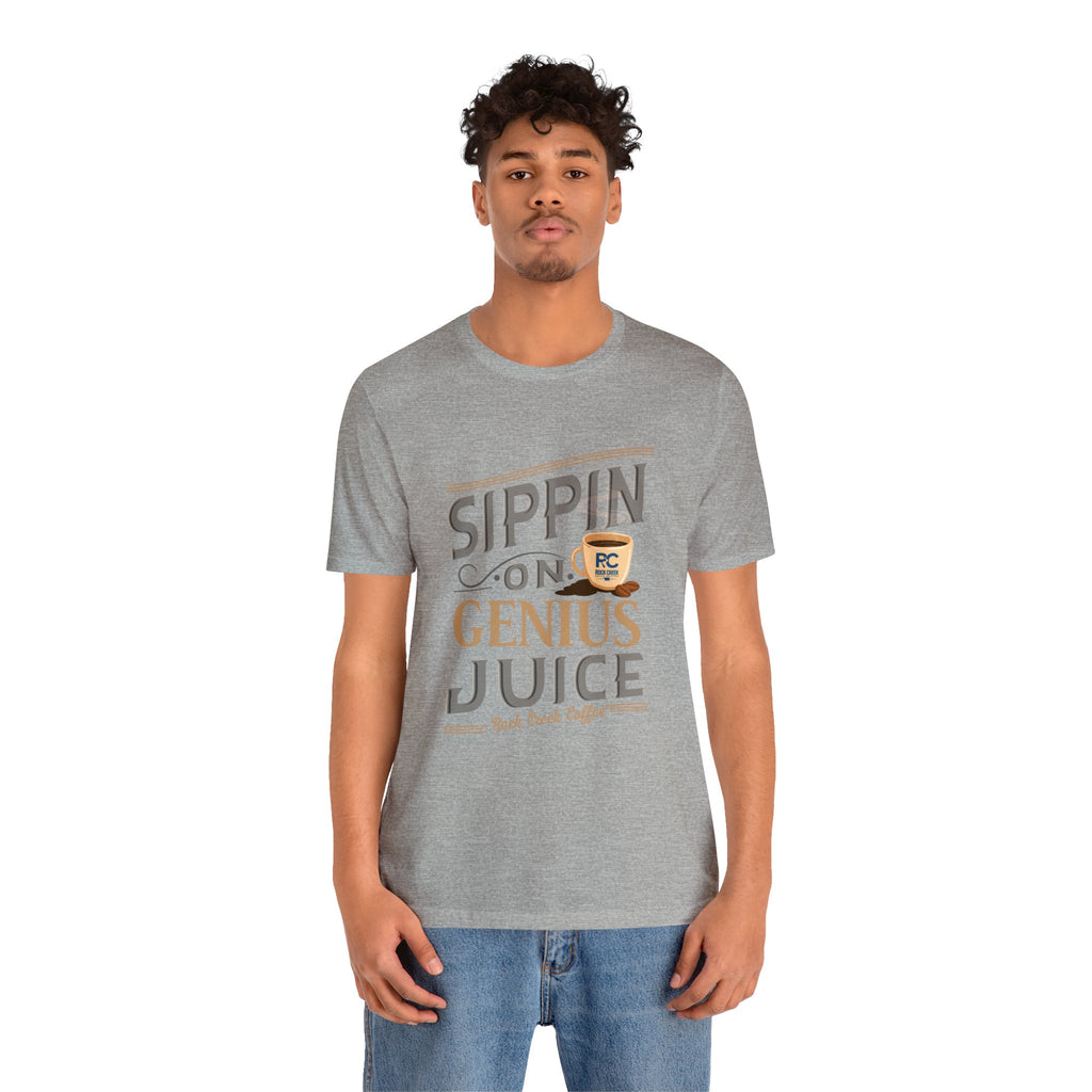 Adult man modeling a heather gray short-sleeve T-shirt featuring the “Sippin on Genius Juice” graphic in bold coffee-inspired lettering with a small cup illustration, shown against a plain white background.