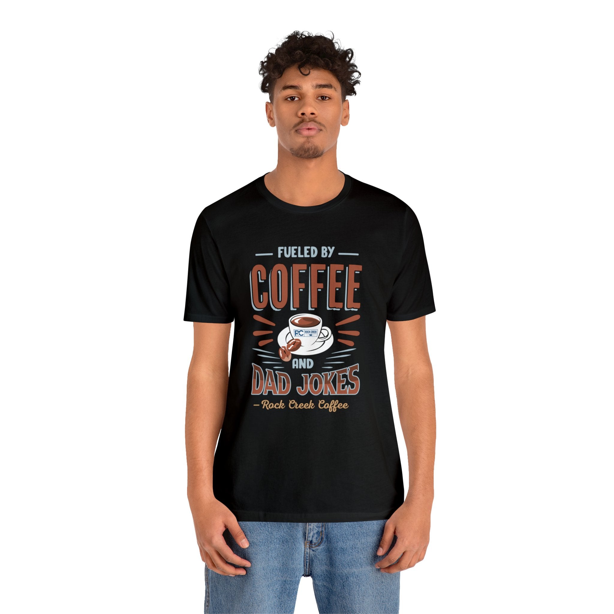 Adult man modeling a black short-sleeve T-shirt featuring the “Fueled by Coffee and Dad Jokes” graphic with a coffee cup illustration and Rock Creek Coffee text, shown against a plain white background.