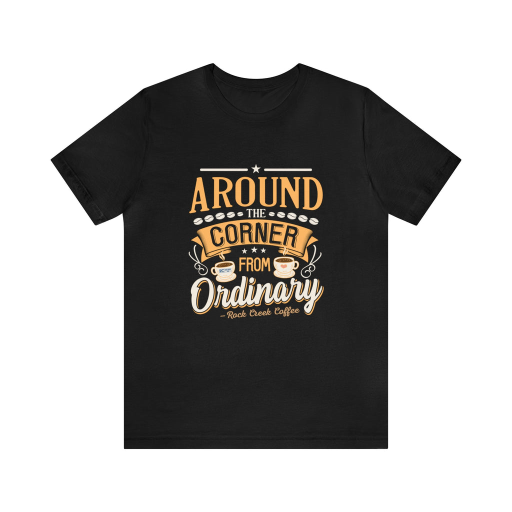 Black short-sleeve T-shirt displayed flat against a plain white background, featuring the phrase “Around the Corner from Ordinary” in a bold coffee-themed typographic design with Rock Creek Coffee branding below.