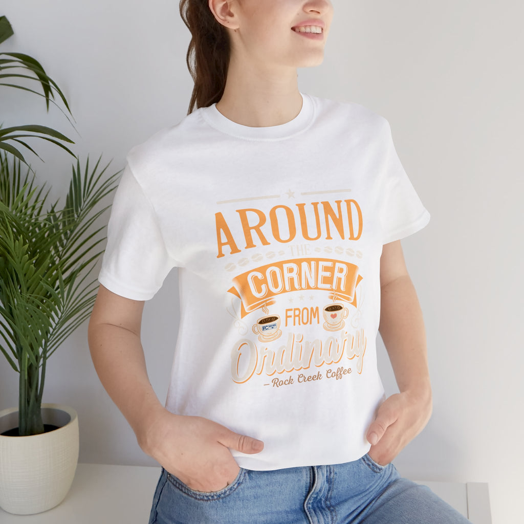 Woman wearing a white Rock Creek Coffee T-shirt with the “Around the Corner From Ordinary” graphic in a casual indoor lifestyle photo