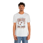 Adult man modeling an ash short-sleeve T-shirt featuring the “Fueled by Coffee and Dad Jokes” graphic with a coffee cup illustration and Rock Creek Coffee text, shown against a plain white background.