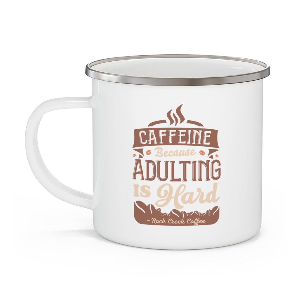 White enamel-style coffee mug with silver rim and side handle, featuring the phrase “Caffeine Because Adulting Is Hard – Rock Creek Coffee” in brown and tan lettering, displayed against a white background.