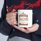 Person wearing a navy holiday sweater holding a white Rock Creek Coffee mug featuring the phrase “Caffeine Because Adulting Is Hard” in brown and tan lettering with coffee bean graphics.