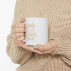 Person wearing a beige knit sweater holding a white Rock Creek Coffee mug with “Sippin on Genius Juice” printed in soft beige lettering and an RC coffee cup graphic.