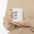 White Rock Creek Coffee mug featuring the phrase “Sippin on Genius Juice” in gray and gold lettering with a small RC coffee cup graphic, held by a person wearing a beige knit sweater with green painted nails against a plain white background.