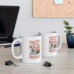 Two white Rock Creek Coffee mugs featuring the colorful “Roasted 818 Miles East of Seattle” design, displayed on a desk with a laptop, binder clips, books, and a small potted plant in the background.