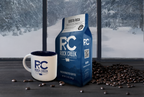 Rock Creek Coffee Roasters Costa Rica medium roast whole bean coffee bag displayed beside a white RC logo mug, with roasted coffee beans scattered on a dark tabletop and a snowy forest scene visible through large windows in the background.