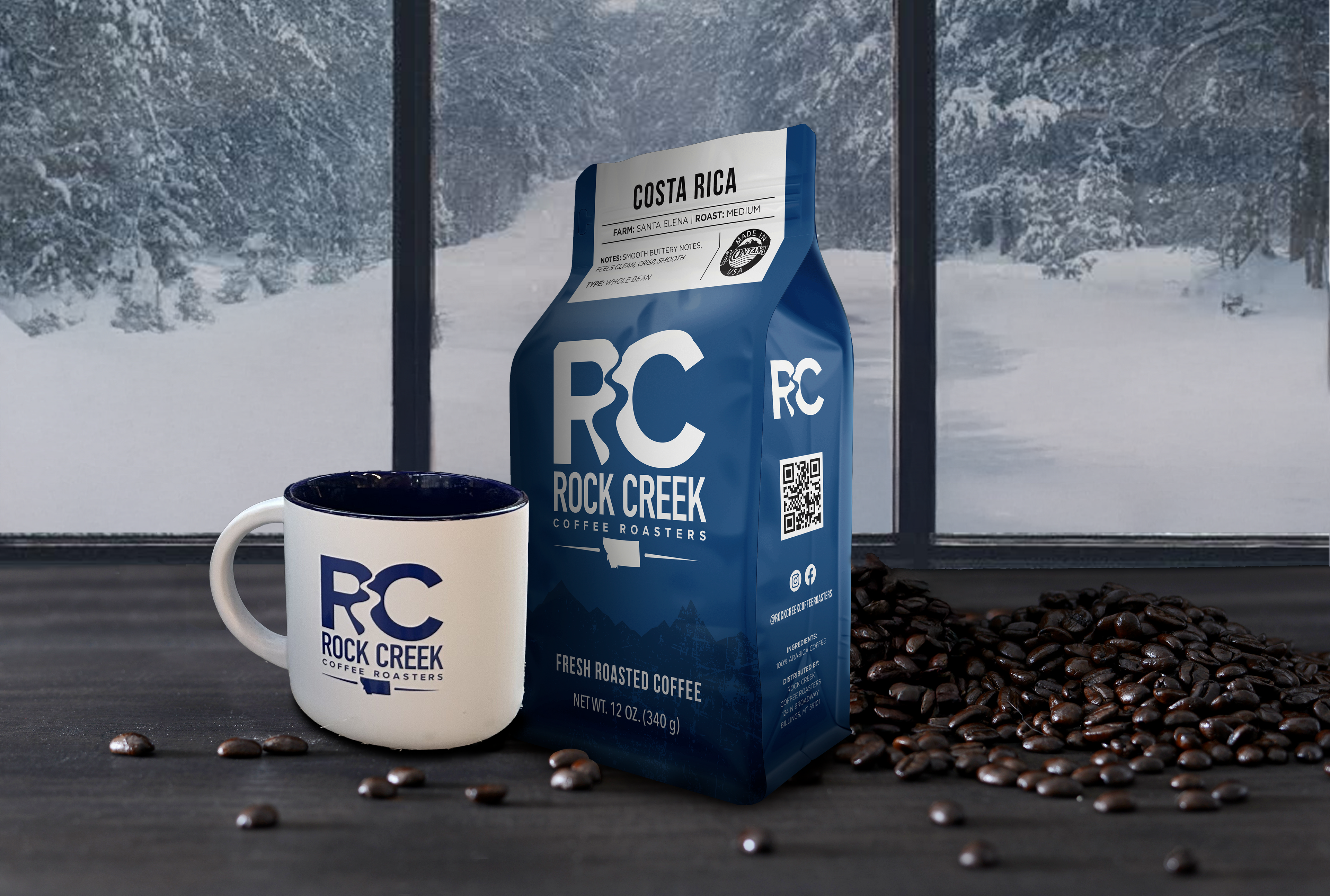 Rock Creek Coffee Roasters Costa Rica medium roast whole bean coffee bag displayed beside a white RC logo mug, with roasted coffee beans scattered on a dark tabletop and a snowy forest scene visible through large windows in the background.