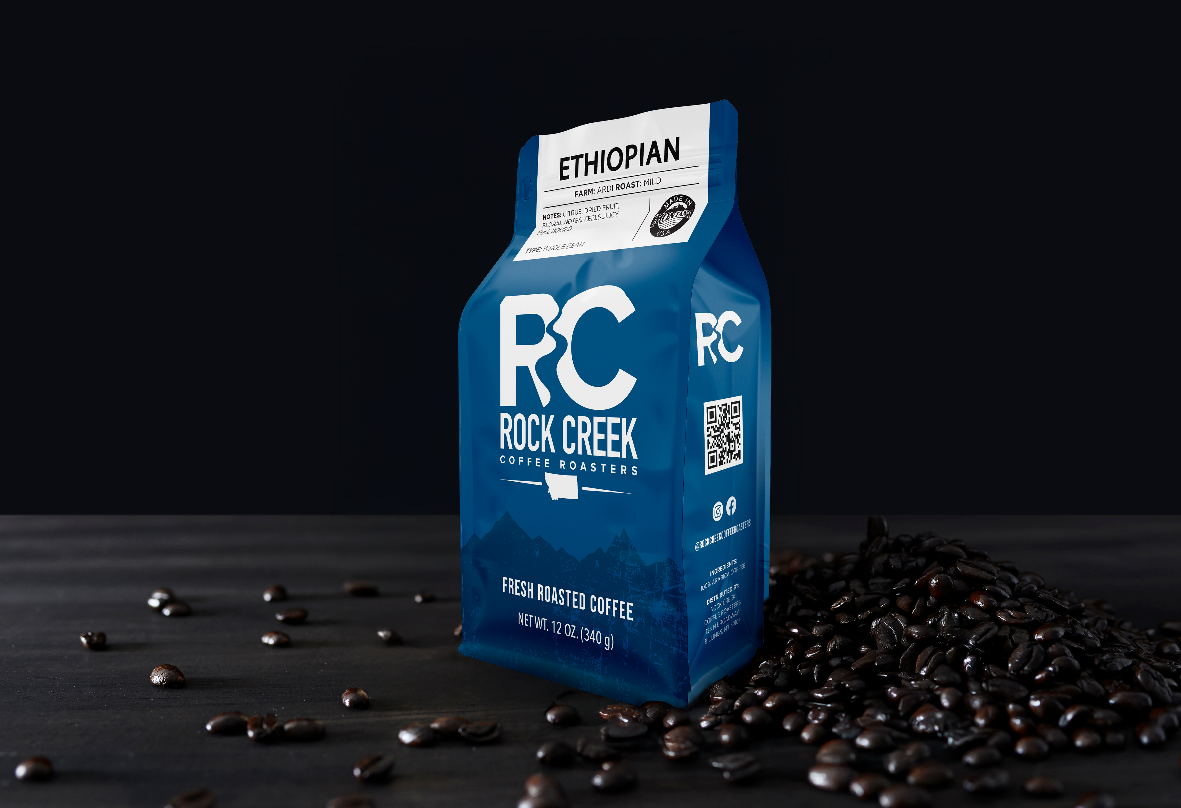 Rock Creek Coffee Roasters Ethiopian Ardi mild roast whole bean coffee bag displayed on a dark tabletop with roasted coffee beans scattered beside it against a black background.