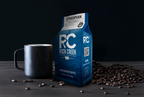 Rock Creek Coffee Roasters Ethiopian Ardi mild roast whole bean coffee bag displayed next to a black ceramic mug, with roasted coffee beans scattered across a dark tabletop against a black background.