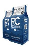 Two blue 12-oz bags of Rock Creek Coffee Roasters whole bean coffee labeled “Your Favorite,” featuring the RCC logo and Montana-inspired mountain design