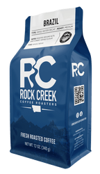 Rock Creek Coffee Roasters Brazil Swiss Water Decaf medium roast whole bean coffee bag, 12 oz, featuring tasting notes of roasted ground nuts and sweet coffee flavor, displayed against a white background.