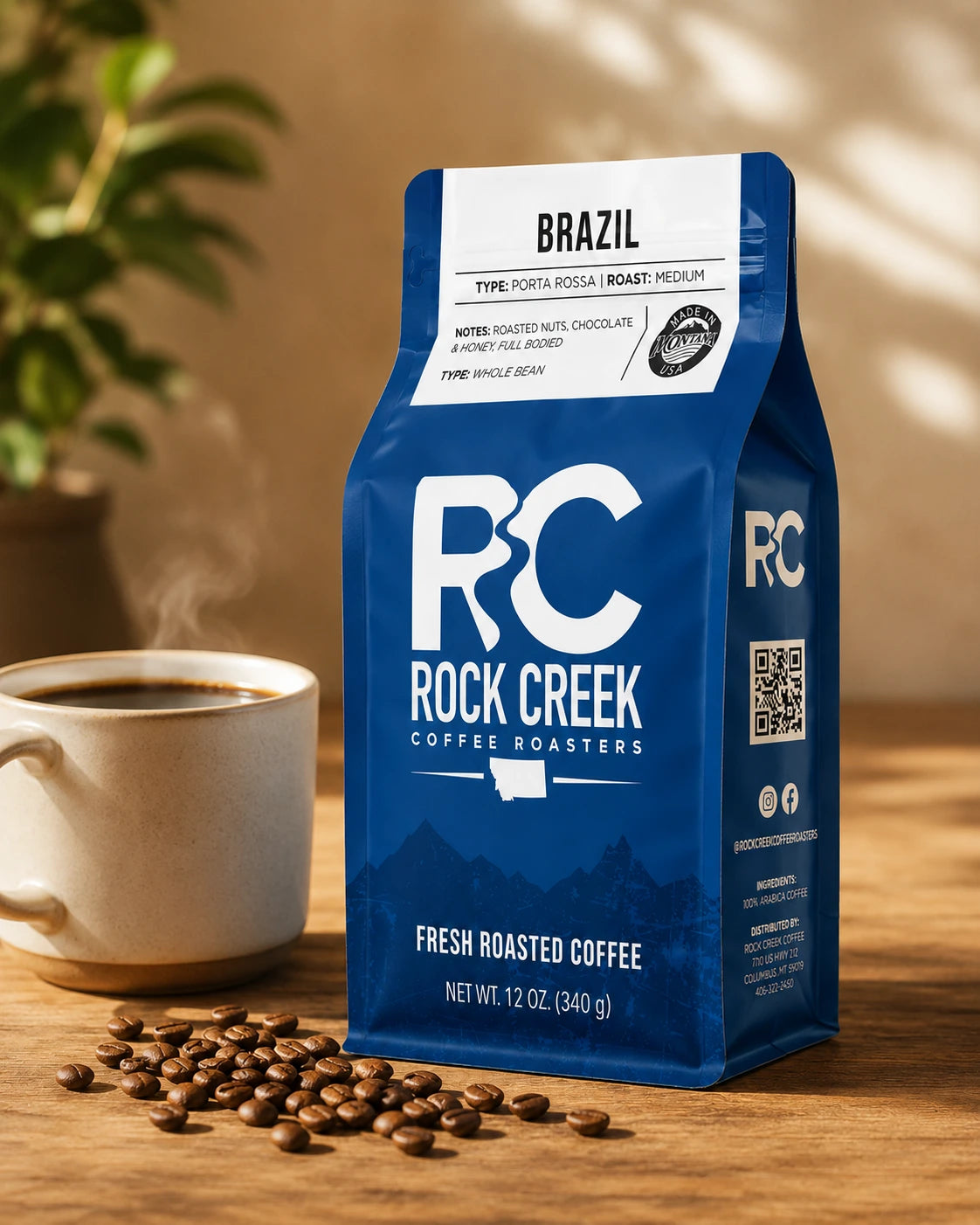 Rock Creek Coffee Roasters Brazil coffee bag displayed beside a steaming cup of coffee and roasted beans on a warm wooden tabletop.