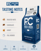Load image into Gallery viewer, Rock Creek Coffee Roasters Brazil coffee bag shown in a tasting notes graphic highlighting roasted nuts, chocolate, honey, and full-bodied flavor notes.