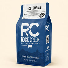 Load image into Gallery viewer, Rock Creek Coffee Roasters Colombian whole bean coffee bag standing upright on a warm ivory background with soft studio lighting.