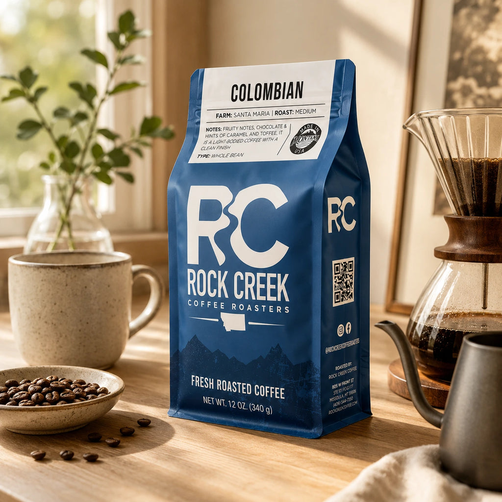 Rock Creek Coffee Roasters Colombian coffee bag in a warm morning coffee setup with brewing tools, roasted beans, and natural window light.