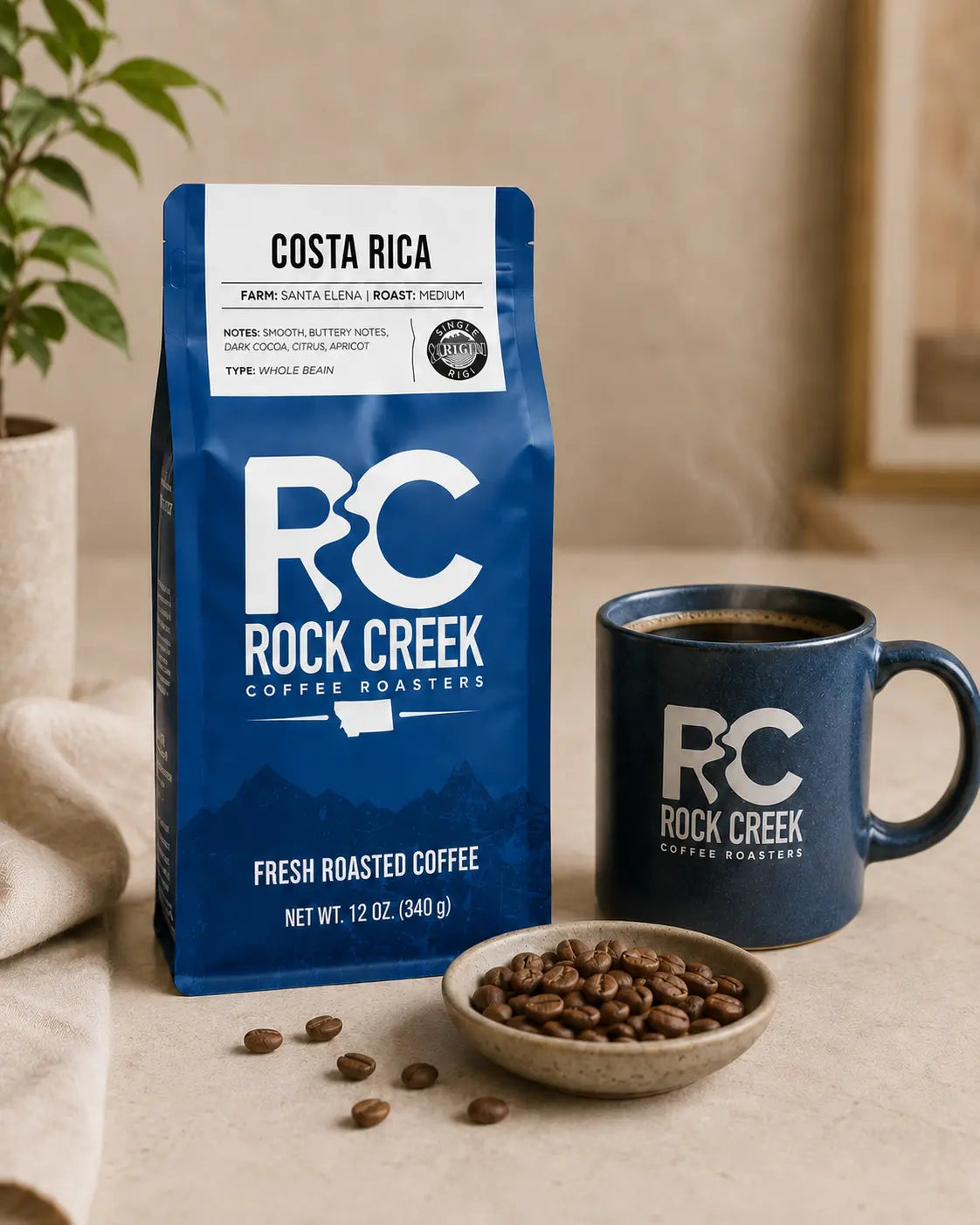 Rock Creek Coffee Roasters Costa Rica whole bean coffee bag beside a branded mug of coffee and a bowl of roasted coffee beans.