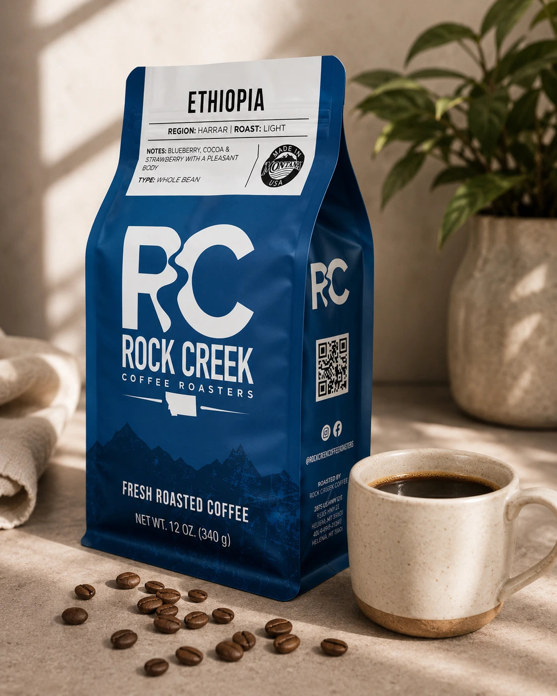 Rock Creek Coffee Roasters Ethiopia coffee bag beside a cup of brewed coffee and scattered beans on a warm neutral tabletop.