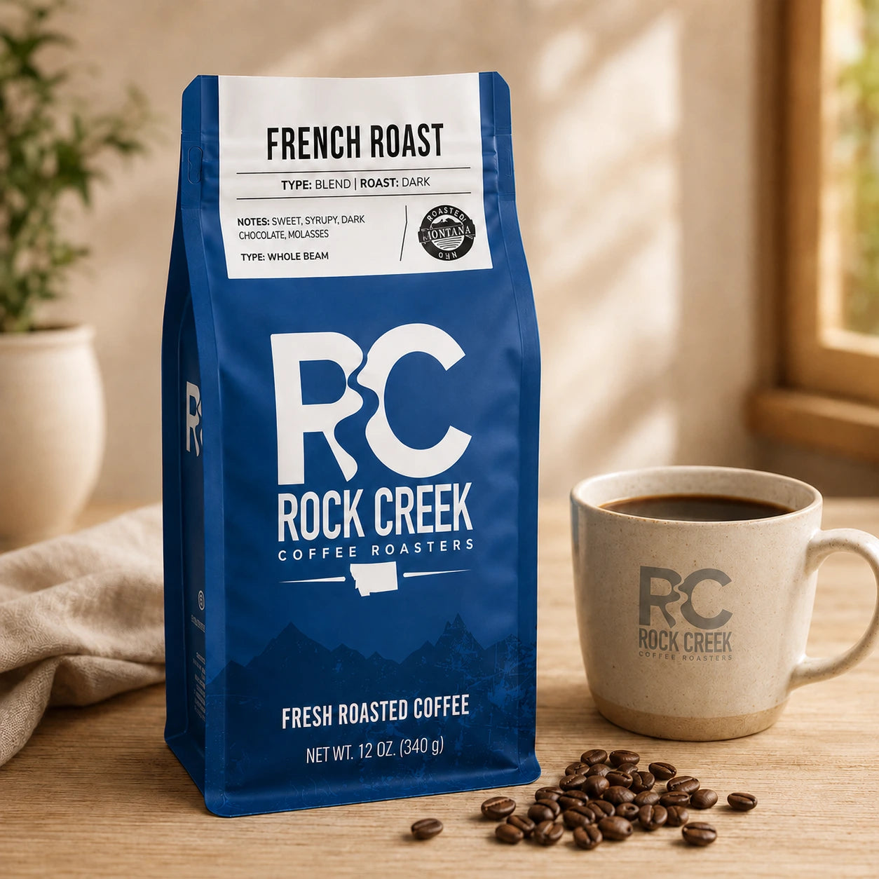 Rock Creek Coffee Roasters French Roast whole bean coffee bag beside a branded coffee mug and roasted beans on a wooden table.