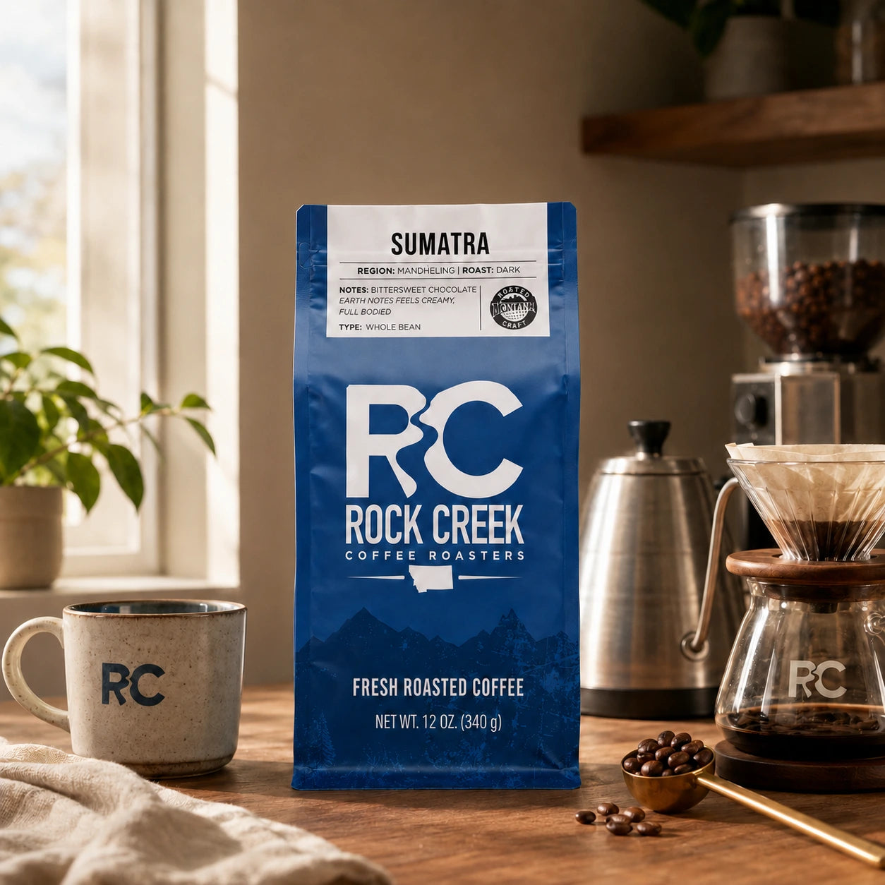 Rock Creek Coffee Roasters Sumatra coffee bag in a warm morning brewing scene with an RC mug, pour-over setup, kettle, grinder, and roasted coffee beans.