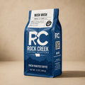 Rock Creek Coffee Roasters Wush Wush coffee bag standing upright on a warm neutral studio background.