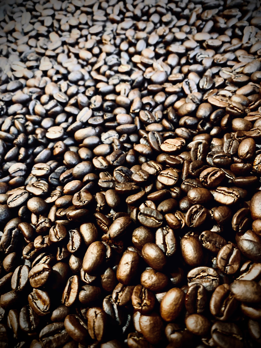 Close-up view of freshly roasted whole coffee beans filling the frame, showing rich brown tones and glossy surfaces.